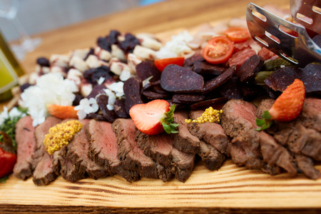 Ham appetizer and meat with strawberry and french mustard, basturma, sausages, pepper on a wooden board in a restaurantの写真素材