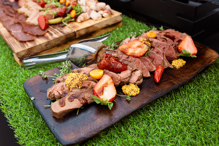 grilled steak with strawberries and french mustard on a wooden board in the restaurantの写真素材
