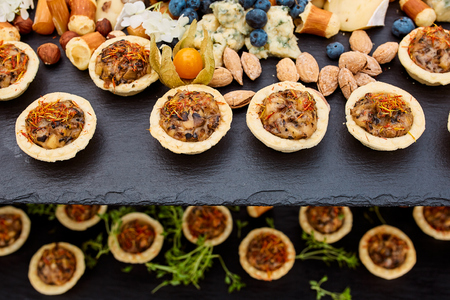 snacks of tartlets with different fillings of figs, cheese, berries with nuts on a ceramic board in a restaurantの写真素材