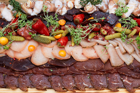 Ham appetizer with basturma, sausages, pepper, cucumbers, on a wooden board in a restaurantの写真素材