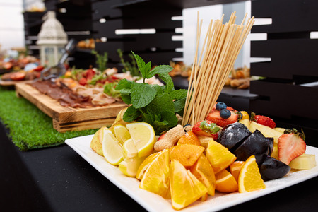 a white plate of oranges, lemons, strawberries, grapes, pears and mint in a restaurant and meat plate on the backgroundの写真素材