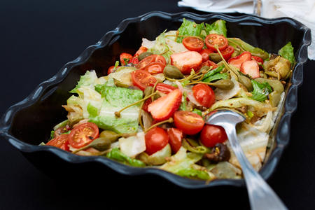 vegetable salad made of tomatoes, lettuce leaves, green olives and strawberries on a black plate in the restaurantの写真素材