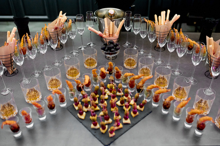 Canapes of shrimp, cheese and vegetables, fruits and breadsticks and empty champagne glasses on a table in a restaurantの写真素材