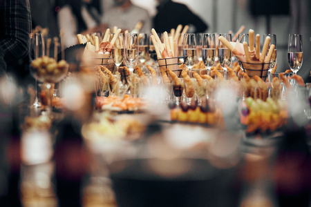 Canapes of shrimp, cheese and vegetables, fruits and breadsticks and empty champagne glasses on a table in a restaurantの写真素材