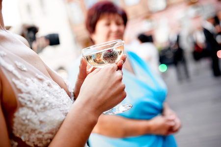 female hands holding a glass of champagne with a frozen berry outside at a weddingの写真素材