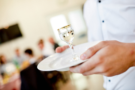waiter's hands hold a white plate on which is a glass of vodkaの写真素材