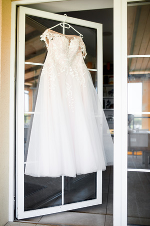white wedding dress hanging on a white hanger on a white doorの写真素材