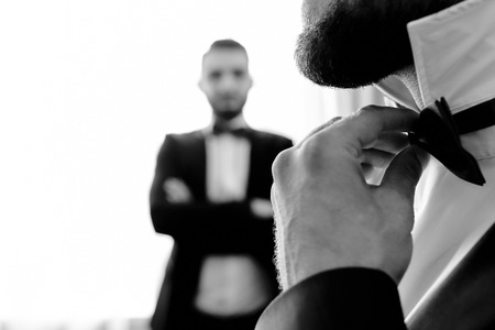 a man with a beard straightens a tie while his friend is watching in the backgroundの写真素材