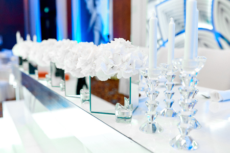flowers in a mirror vase next to small and big candles on a table at a weddingの写真素材