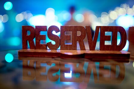 A brown wooden plate stands directly in a cafe-restaurant, on a glass table and reserves a place for certain guests of the institution on a blue backgroundの写真素材