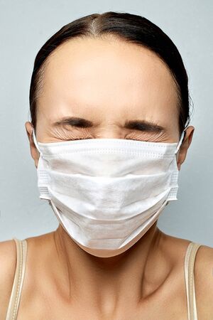 brunette in white disposable medical mask in fear closed her eyes over gray backgroundの写真素材