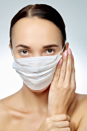 young brunette girl looking forward; she is wearing a white medical mask; near her face, well-groomed hands clasped next to himの写真素材