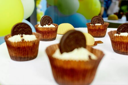 chocolate cake with chocolate biscuits with top and white cream stand on a plate in an individual package. In the background festive colorful balloonsの写真素材