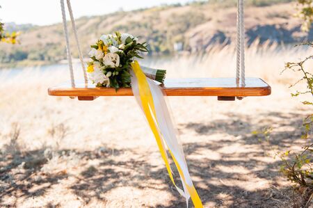 Wedding decoration of a beautiful delicate bouquet lying down on a swing in the park against green backgroundの写真素材