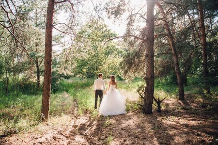 bride and groom is running with joined hands on a city park road sunshineの写真素材