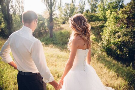 bride and groom is running with joined hands on a city park road sunshine