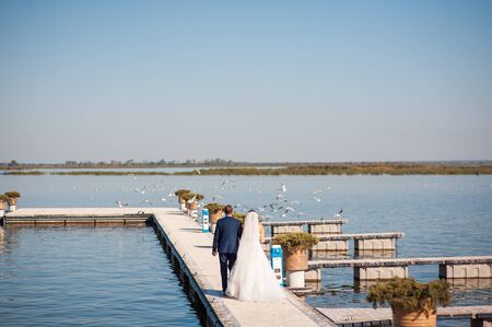 bride and groom is running with joined hands on the pier sunの写真素材