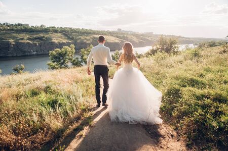 bride and groom is running with joined hands on a city park road sunshineの写真素材