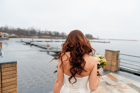 bride in a white dress with a chic hair goes to the river pierの写真素材