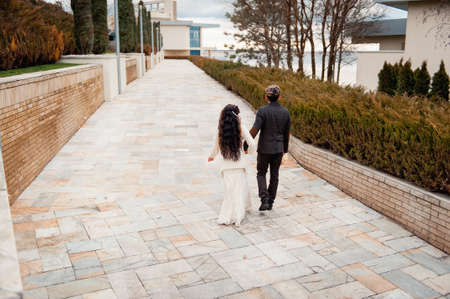 bride and groom is running with joined hands on a city park roadの写真素材