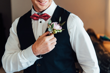 groom clasping stylish watch band on his wrist and bow tie