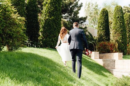 bride and groom is running with joined hands on a city park road sunshineの写真素材