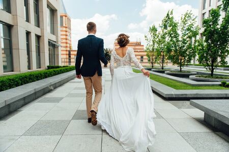 bride and groom is running with joined hands on a city park road sunshineの写真素材