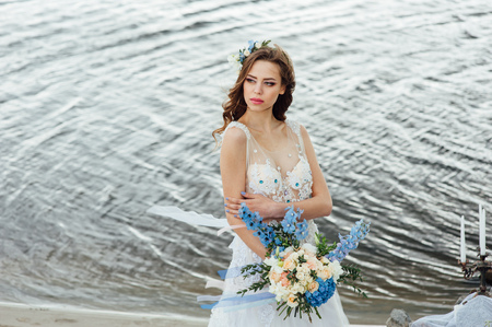 Beautiful young bride woman in luxury wedding dress with red lips makeup and long wavy hairstyle. Beauty girl portrait posing near water, outdoor photo.の写真素材