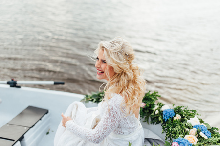 Beautiful young bride woman in luxury wedding dress with red lips makeup and long wavy hairstyle. Beauty girl portrait posing in the boat, outdoor photo.の写真素材