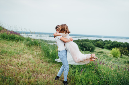 Happy Bride and groom walking on the green grass near the river, smiling and kissingの写真素材