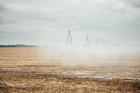 Mobile irrigation pivot watering on an empty field. Farmer watering the field after a successful harvest on a cloudy dayの写真素材