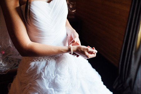 Wedding. Bride. Preparations. Wedding Dress. Bride in cream-colored dress stands in front of the window with her hands foldedの写真素材