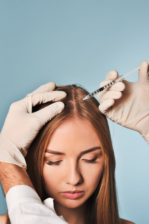 Handsome woman receives an injection in the head. The procedure makes male doctor in white gloves. The concept of mesotherapy. Thrust to strengthen the hair and their growthの写真素材