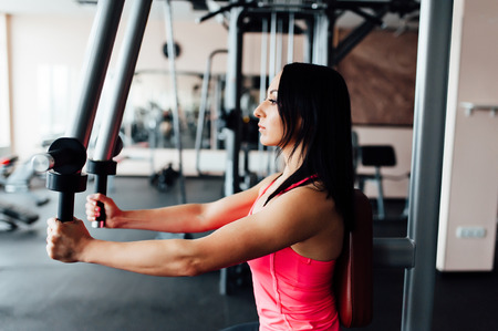 Athletic young woman doing exercises on the simulator for the upper muscle groups