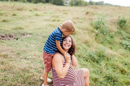 Pregnant woman sitting countryside with her son. Child hugging his pregnant mother.
