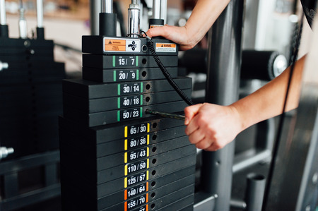 Fitness equipment in the gym. Sport girl adjusts the required weight for a workout. Black weight for...