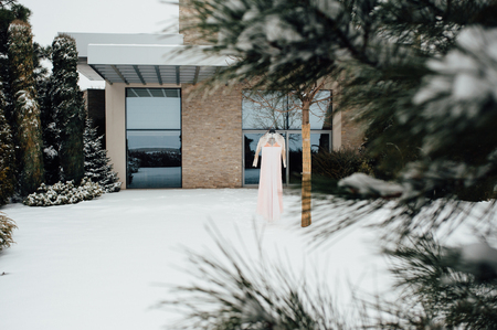 a beautiful pink wedding dress hanging on the tree near the house with large windowsの写真素材