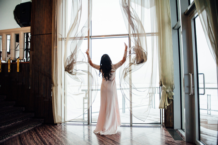 beautiful woman opens her arms curtains in the house with huge panoramic windowsの写真素材
