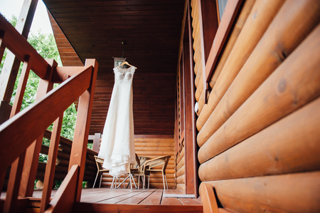 beautiful white wedding dress hanging on the wall of the house made of wooden beamsの写真素材