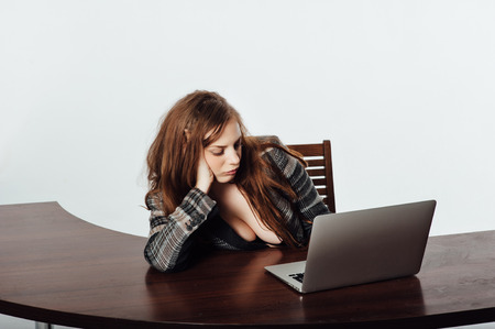 Sexy business woman in a jacket with a big neckline and chest sits on a chair and works with a laptopの写真素材