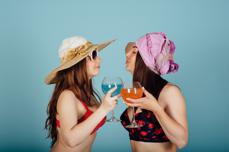 Two beautiful young women in bikini relaxing together and smiling. Girls are happy with rest and drink cocktails from a glass gobletの写真素材