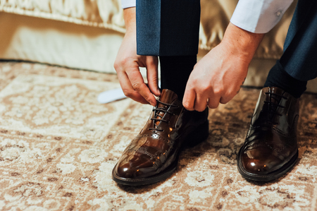 Close-up young man tying elegant shoes indoorsの写真素材