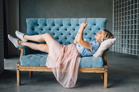 Beautiful woman is lying on the couch with phoneの写真素材