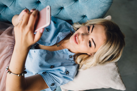 Beautiful woman is lying on the couch with phoneの写真素材