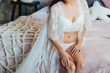 Beautiful bride in lingerie and white dress. charming girl shows her sexy legsの写真素材