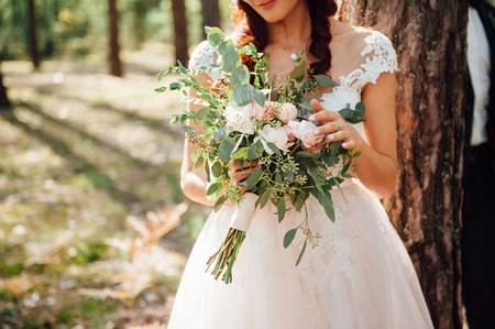 bride in a white dress holding a bouquet of flowers and greeneryの写真素材