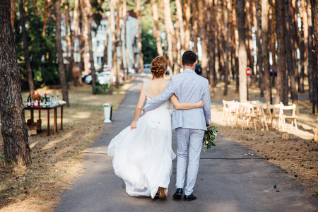 bride and groom is running with joined hands on a city park road sunshineの写真素材