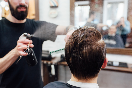 Close up shot of man getting trendy haircut at barber shop. The male hairstylist in tattoos serving client.の写真素材