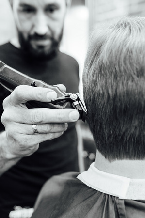 Close up shot of man getting trendy haircut at barber shop. The male hairstylist in tattoos serving client.の写真素材