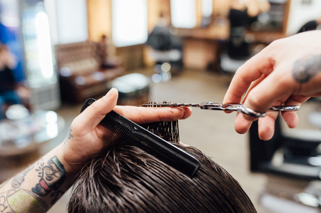 Close up shot of man getting trendy haircut at barber shop. The male hairstylist in tattoos serving client.の写真素材